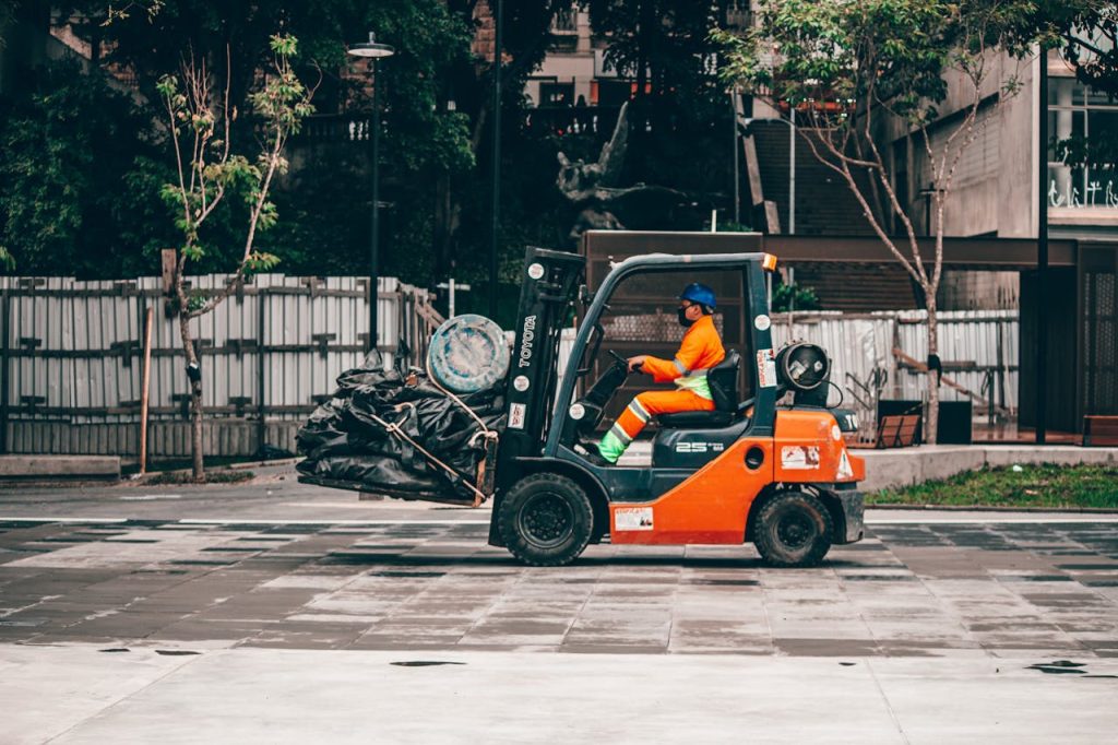 pexels photo 6026765 A man operates a forklift carrying rubbish in an urban environment, showcasing industrial logistics.